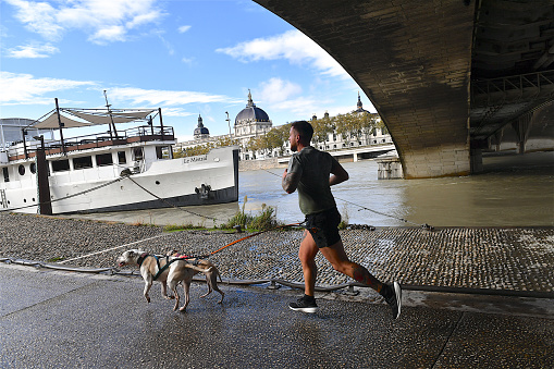 Lyon, France-11 04 2023: Young man running with his dogs along the Rhône river with the building of the Hotel-Dieu in the background, Lyon, France.