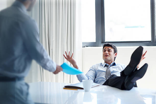 What's the problem?! An irritated businessman with his feet up on his desk as a coworker stands by arrogance stock pictures, royalty-free photos & images