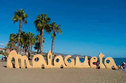 Málaga, Spain - 20th October 2023: The sign on Malaguena Beach, the largest beach in Málaga, Spain, under a clear, blue sky on a warm, late-October afternoon. There are some incidental people on the beach.