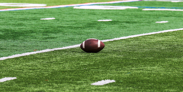 One American football resting on a green turf field with room for copy space.