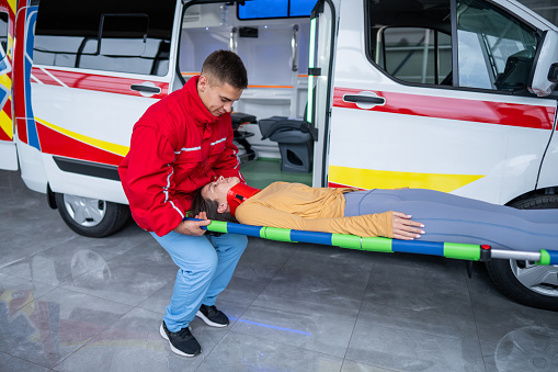 Paramedic transporting female accident victim with neck injury on stretcher to ambulance