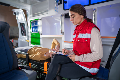Female doctor taking notes while examining young female patient in ambulance vehicle
