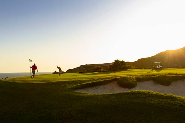 A couple playing golf on a putting green Landscape image of two golfers playing while in the green of a golf course. putting golf stock pictures, royalty-free photos & images