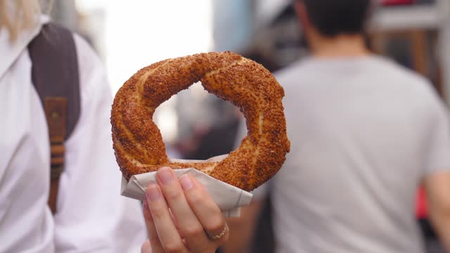 Girl tourist holding simit close-up on city street on sunny day without face.