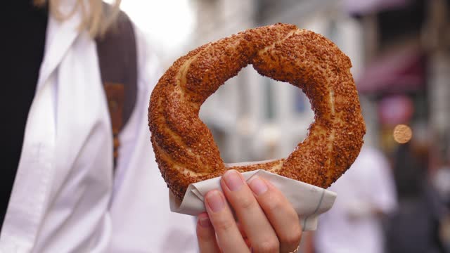 Girl tourist holding simit close-up on city street on sunny day without face.