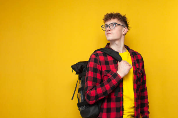 istock curly guy student in glasses with a backpack stands on a yellow background, looks back at copyspace and smiles 1793424785