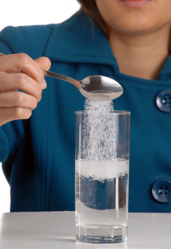 Woman pouring sugar on glass water.