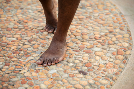 A South Indian man's feet walk over acupressure stones in a public park.