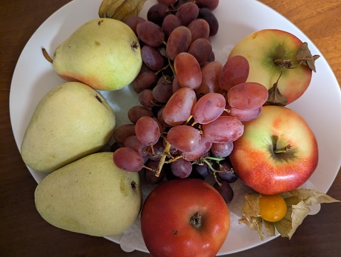 A plate of apples, pears and grapes on the table.