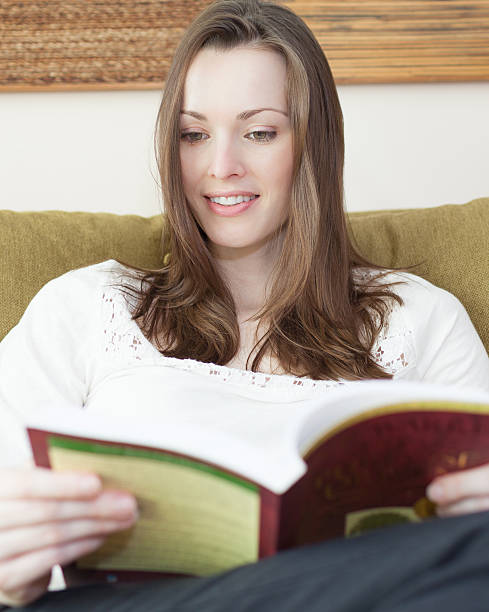 istock Young woman reading book on couch 179348505