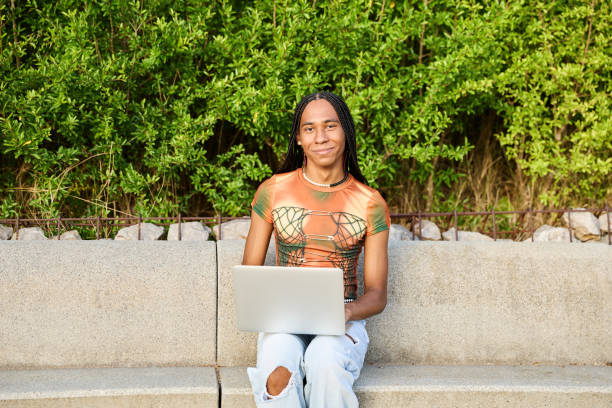 istock Non-binary person working on laptop sitting on city bench looking at camera smiling 1793487811
