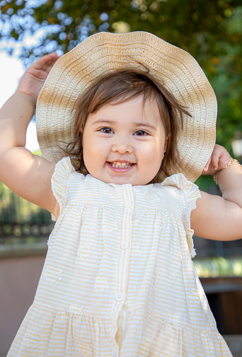 Young girl, baby or toddler playing outside wearing a hat with a wide brim. Happy smiling laughing girl playing on equipment, climbing, at daycare or day care. Happy child playing in the backyard.
