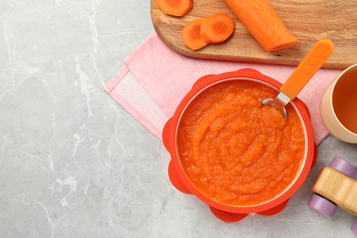 Healthy baby food. Bowl with delicious carrot puree on light grey marble table, flat lay. Space for text