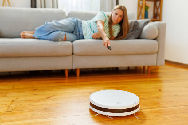 istock Robot vacuum cleaner cleaning a room while a woman relaxes on the sofa 1793532015