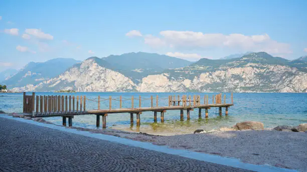Wooden pier on the shore of Lake Garda near Malcesine in Italy. On the horizon mountains of the Alps