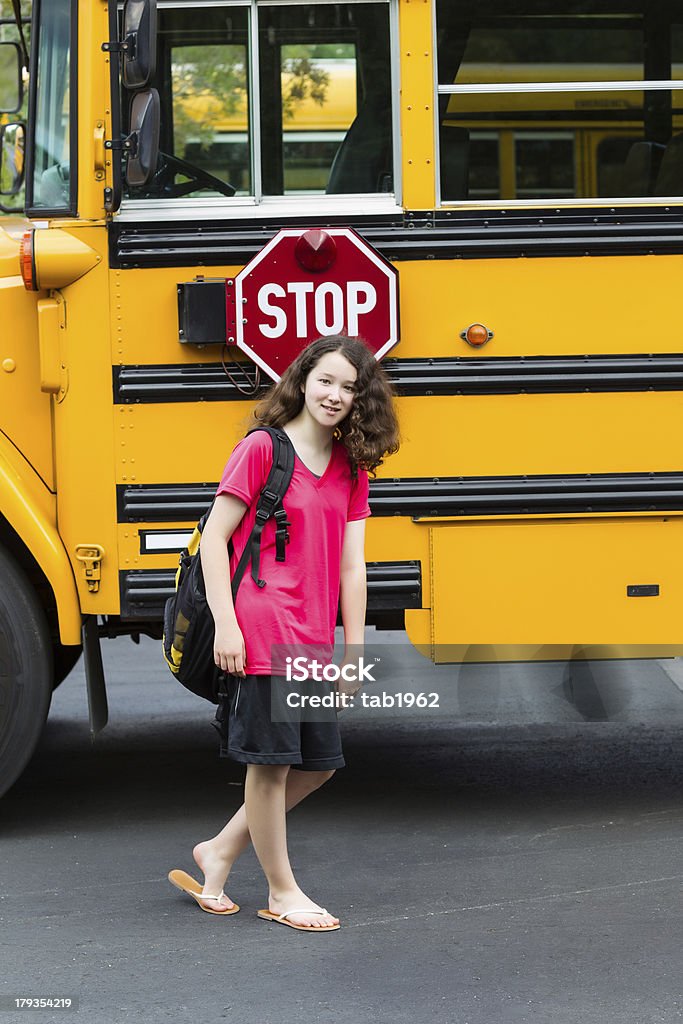 Young Girl Student back in Grade School Vertical photo of young girl standing by side of school bus, with back pack over her shoulders, wearing sandals while looking forward Adolescence Stock Photo