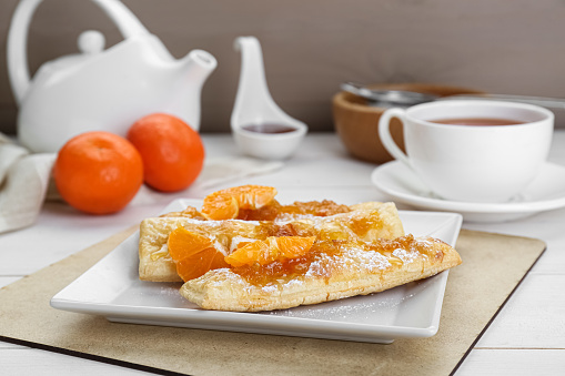 Fresh tasty puff pastry with sugar powder and tangerines on white wooden table, closeup