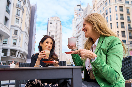 couple of mature women having a coffee on the terrace of a bar in the city. friends enjoying a hot drink while talking and laughing