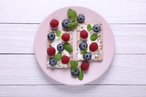 Plate with crispbreads, berries and mint on white wooden table, top view