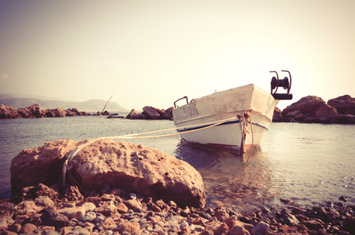Typical greek small boat in the sea anchored to a rock. Elaborated image for the vintage mood.