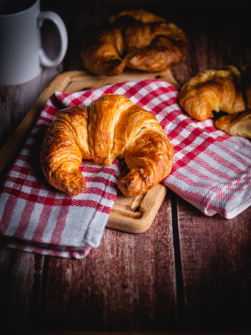zenithal view of a handmade natural croissant on a wooden table with a red checkered tea towel