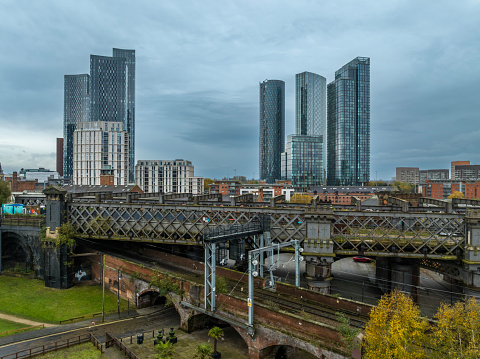 An aerial photograph of skyscrapers in downtown Manchester, England. The photograph was produced on an overcast day during autumn. Victorian railway network and iron bridge can be seen in the foreground.