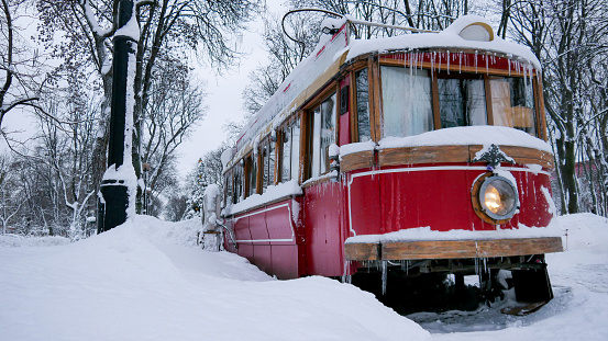 old red tram stuck on the winter road. Public transport covered in snow. Bad weather condition, cold winter blizzard