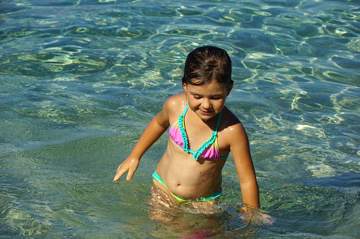 Adorable little girl is playing in the shallow turquoise sea