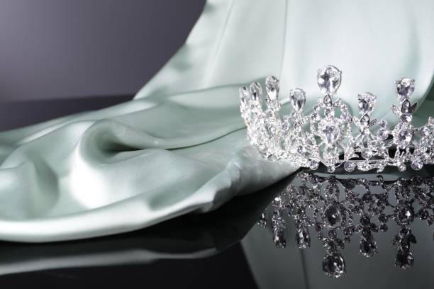 istock Beautiful silver tiara with gems near light cloth on dark mirror surface. Space for text 1793615847