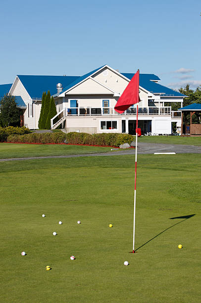Golf course clubhouse and practice green with flag and golfballs.