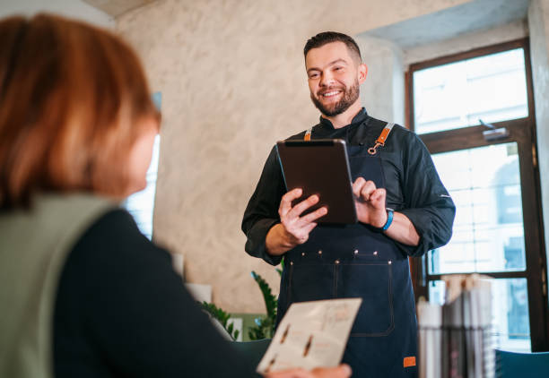 istock Smiling Caucasian man waiter taking orders from Female client with digital tablet in cafe restaurant. Happy people, restaurants, fastfood and foodservice industry, small business concept image. 1793618480