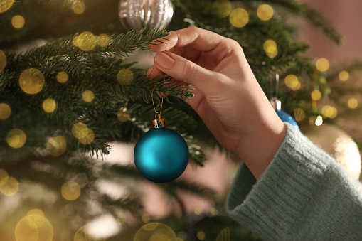 Woman decorating Christmas tree with beautiful light blue bauble, closeup