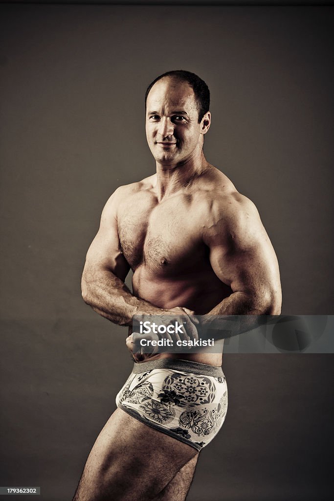 Bodybuilder posing Bodybuilder posing over gray background -colorized photo for dramatic mood Flexing Muscles Stock Photo