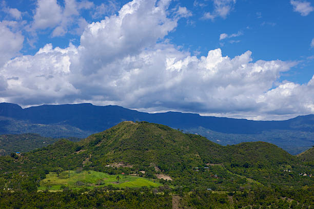 The Andes Mountains as viewed from the town of Anapoima, in the Cundinamarca Department in Colombia, South America. A green patch of land without any trees adds interest to the photo.  Blue skies and dramatic white clouds complete the picture. Photo shot in the afternoon sunlight; horizontal format. Copy space, No people.