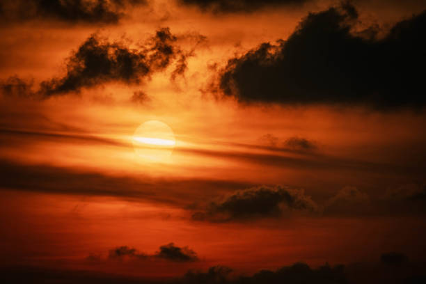 Scenic red orange Sunset with Sun hiding in clouds, glowing light line crosses Sun disk horizontally, close up photo. Thailand