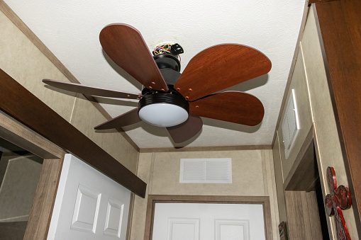 View on brown ceiling fan with five blades made from plastic installed in hotel room for supporting air condition. Walls are painted yellow and there are also white ceiling and black television.