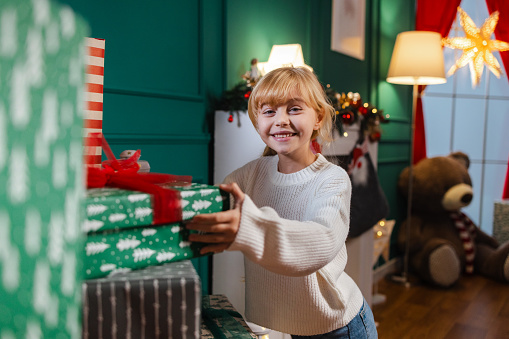 Portrait of a cheerful little girl arranging Christmas presents wrapped with New Year's wrapping paper