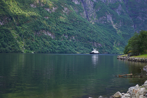 Small local ferry boat in the beautiful fjord during calm summer evening in Norway. Very common and neccesary kind of public boat transport in the norwegian fjords and between islands on the coast.