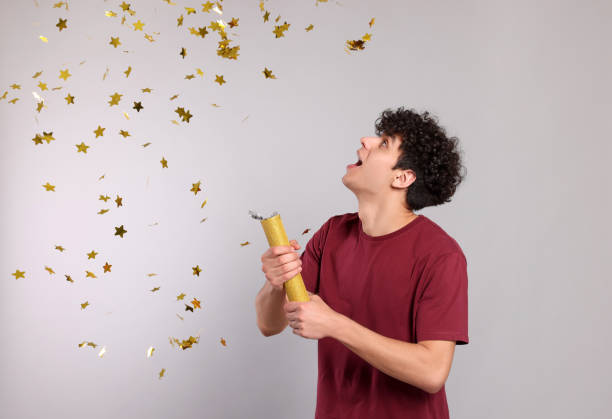 istock Emotional young man blowing up party popper on light grey background 1793722858