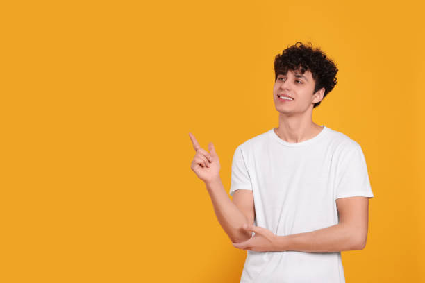 istock Handsome young man pointing at something on orange background. Space for text 1793723372