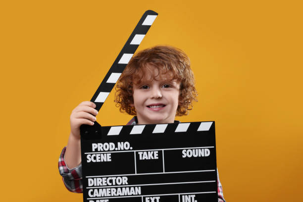 istock Smiling cute boy with clapperboard on orange background. Little actor 1793725008