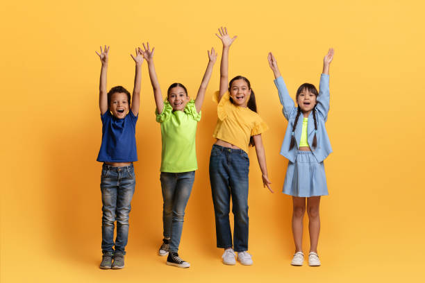 Cool diverse kids raising hands up on yellow background