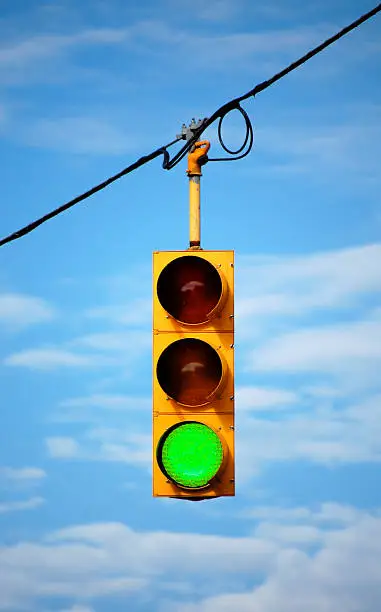Suspended stoplight showing green, with sky background