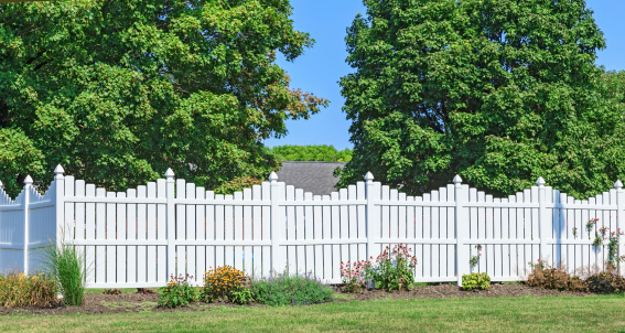 New white vinyl fence with nice yard landscaping and trees in the back ground.