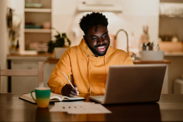 istock A cheerful interracial man is writing down notes while smiling at the laptop late at night from home. 1793784014