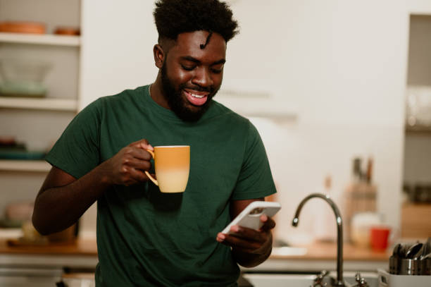 istock A cheerful interracial guy is standing in the kitchen at home, enjoying coffee and reading messages on the phone. 1793784018