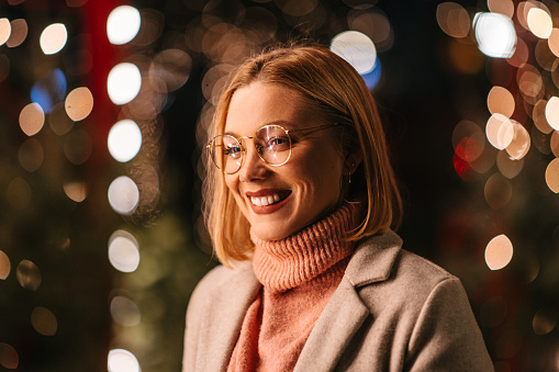 A portrait of a woman in warm clothing in front of Christmas lights outdoor