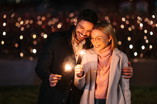 The man and a woman are holding sparklers and celebrating the New Years Eve. Christmas lights as a background