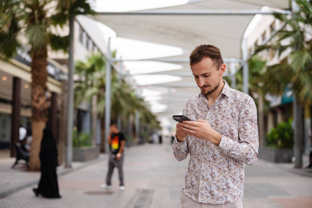 istock Handsome young man using his smart phone while walking in a city 1793830905