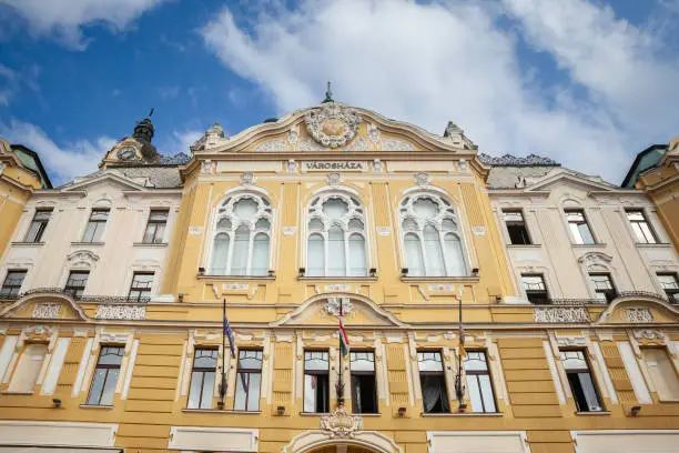 Picture of the Pecs city hall. The town hall of Pécs is the seat of the general assembly of the city of Pécs county, and it is also one of the most characteristic buildings of Széchenyi tér . The building is the third building in the series after the end of Turkish rule - the first one was built in 1698 , then in 1710 the building, which was significantly damaged by fire, was rebuilt in its original form. In 1834 , a two-story classicist town hall was built in its place, and the current neo-baroque building was completed in 1907 based on the plans of Adolf Láng .